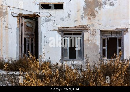 Neglected building facade with broken windows, blue window shutters and doors in Al Jazirah Al Hamra haunted town in Ras Al Khaimah, United Arab Emira Stock Photo