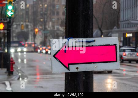 A sign pointing left to a filming location, attached to a traffic light pole on Hastings Street. Behind it, a traffic light is also pointing left. Stock Photo