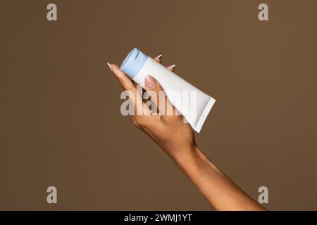 Female hand holding cream tube cosmetic products on a yellow background ...