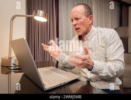 older senior man frustrated working on his computer in a hotel room Stock Photo