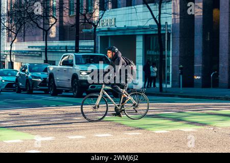Vancouver, Canada - Feb 16 2024: A man riding his bicycle and crossing Dunsmuir Street on the bike lane, with cars stopped at the traffic light. Stock Photo