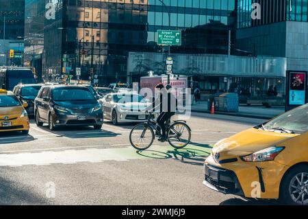 Vancouver, Canada - Feb 16 2024: A woman riding her bicycle is crossing Georgia Street using a bike lane, while cars are stopped at the traffic light. Stock Photo