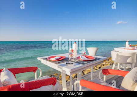 Relaxing outdoor restaurant at the beach. Table setting at tropical beach restaurant. Elegant white wooden tables chairs under beautiful soft sunlight Stock Photo