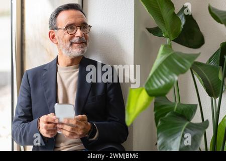 Senior businessman in a smart jacket and glasses using his smartphone Stock Photo