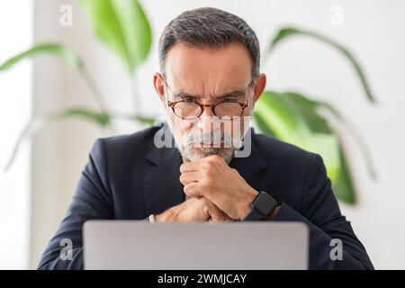 Concentrated mature businessman with glasses deep in thought, resting chin on hands Stock Photo