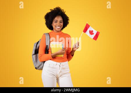 Smiling young woman with afro hair, dressed in an orange sweater and white jeans Stock Photo