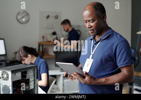 Serious male technician with tablet standing in front of camera in coworking space and looking through online instructions Stock Photo