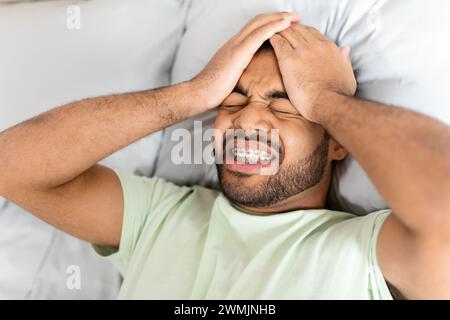Irritated young black guy touching his bed, laying in bed Stock Photo
