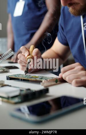 Close-up of young technician of maintenance service using electric handtool while repairing part of computer processor by workplace Stock Photo