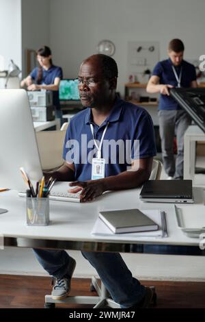 Experienced male engineer of repair service center looking at screen of desktop computer while sitting by workplace in coworking space Stock Photo