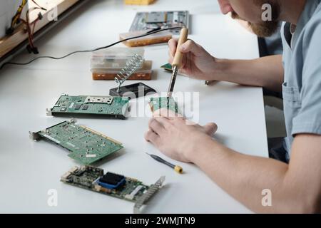 Hands of young male technician of troubleshooting office repairing computer motherboard with electric transmission tweezers Stock Photo