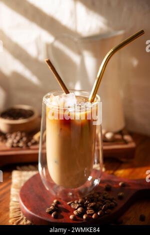 Iced coffee served in a double-walled glass cup and metal straw, a cold summer drink prepared with ice cubes and spices, cinnamon, nutmeg, vanilla, mu Stock Photo