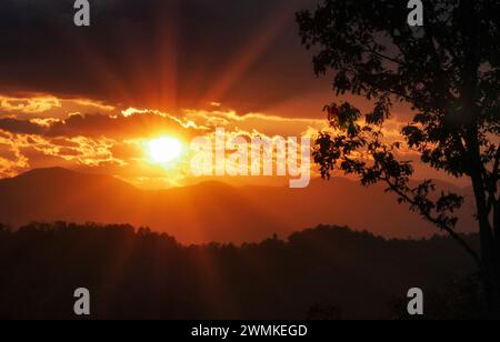 Sun sends out rays of light as it sets over the Blue Ridge Mountains silhouetted in the distance Stock Photo