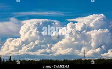 Large storm clouds forming on the horizon behind large power transmission lines on a warm summer evening; Edmonton, Alberta, Canada Stock Photo