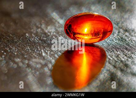 Close up of a glowing gel capsule with a sun glow inside on a grey slate background; Studio Shot Stock Photo