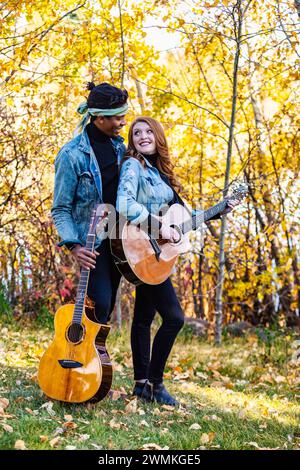 Mixed race married couple, looking at each other smiling and holding guitars during a fall family outing in a city park, spending quality time toge... Stock Photo