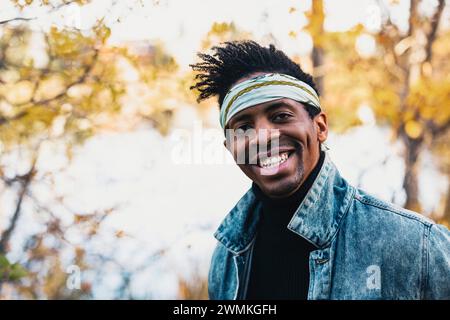 Close-up portrait of a handsome man wearing a bandanna headband, smiling at the camera in a city park in the Fall; Edmonton, Alberta, Canada Stock Photo