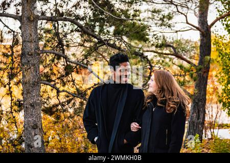 A mixed race couple smiling at each other walking through the woods, spending quality time together during a fall family outing in a city park Stock Photo