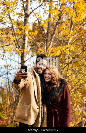 Close-up of a mixed race married couple taking a selfie together while spending quality time together during a fall family outing in a city park Stock Photo