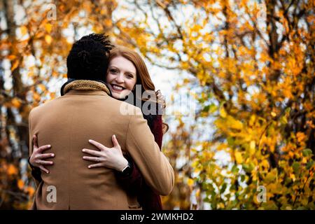 View taken from behind of a mixed race married couple hugging each other with wife smiling at the camera, while spending quality time together duri... Stock Photo