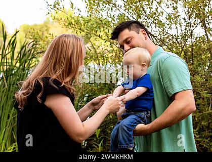 Mother and father playing with their young son who has Down Syndrome, in a city park during a warm fall afternoon; Leduc, Alberta, Canada Stock Photo
