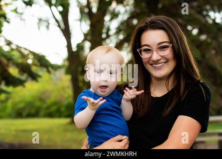 Outdoor portrait of an older sister spending quality time with her young brother who has Down Syndrome, in a city park during a warm fall afternoon Stock Photo