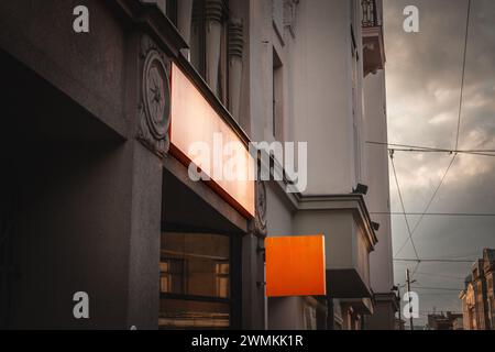 An empty, vibrant orange square signboard, prominently displayed and hanging from a metal bracket against a building facade, captures the essence of u Stock Photo