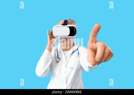 Mature female doctor in VR glasses using virtual screen on blue background Stock Photo