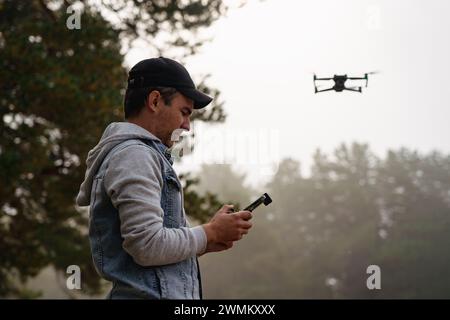 Professional photographer taking photos from drone. man taking aerial photos in forest. Man controlling his drone on background of mountain forest. Stock Photo