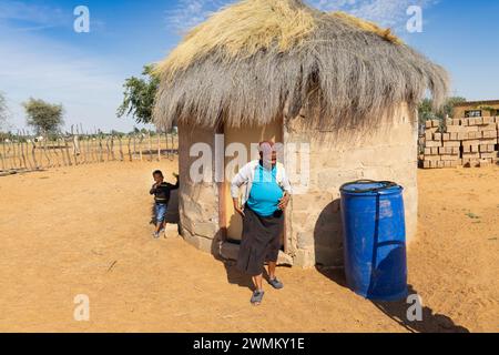 village african woman in front of a shack with thatched roof, in a sunny day outdoors Stock Photo