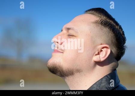 Young attractive man enjoying the sun in a park with eyes closed Stock Photo