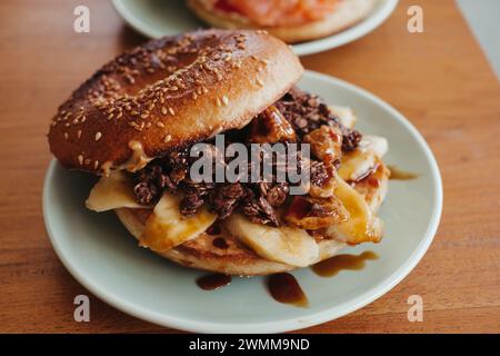 A halved bagel breakfast sandwich with scrambled eggs, spinach, and cheese on a plate and on a wooden table Stock Photo
