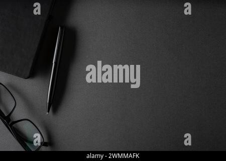 Top view of ballpoint pen, glasses and notepad lying on dark gray table Stock Photo