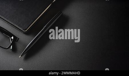 Top view of ballpoint pen, glasses and notepad lying on dark gray table Stock Photo