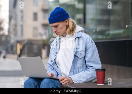 Stylish hipster guy sitting in urban street, working online, searching info in laptop computer Stock Photo