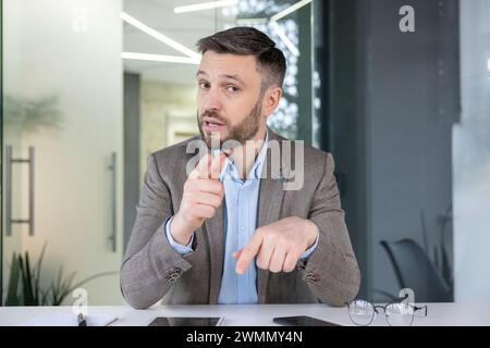 Professional male executive points and explains concepts during a corporate meeting in a modern office setting. Stock Photo