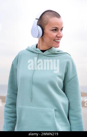 Vertical Close-up smiling sporty woman with headphones looking at the camera outdoors. Stock Photo