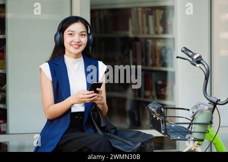 Smiling asian businesswoman hold reusable eco-friendly ecological cup and using mobile while sitting at park Stock Photo