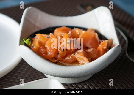 A bowl of salmon tartare with sesame and herbs close up.Healthy vegetarian food, raw salmon meat. Delicious asian dish served on restaurant table Stock Photo