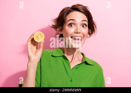 Photo portrait of lovely young lady hold half lemon lick teeth dressed stylish green garment isolated on pink color background Stock Photo