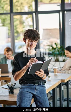 Curly-haired man with glasses smiling and taking notes in a dynamic office space, startup ideas Stock Photo