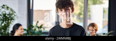 happy and curly-haired man smiling and taking notes in a dynamic office space, startup banner Stock Photo