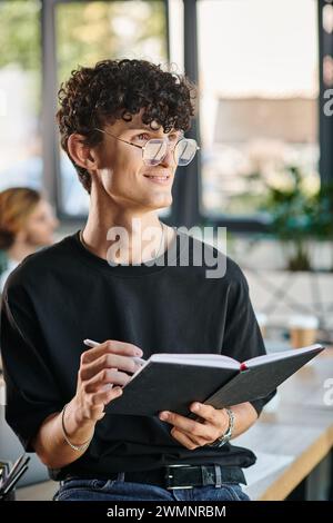 Curly-haired startup team member with glasses smiling and taking notes in a dynamic office space Stock Photo