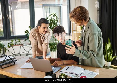 Three young professionals discussing a project and looking at smartphone while creating startup Stock Photo