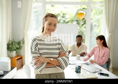 Portrait of happy young project manager standing in office of small IT company Stock Photo
