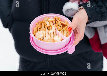 A woman's hand holds a pink box of crackers. Snack in the fresh air.  Stock Photo