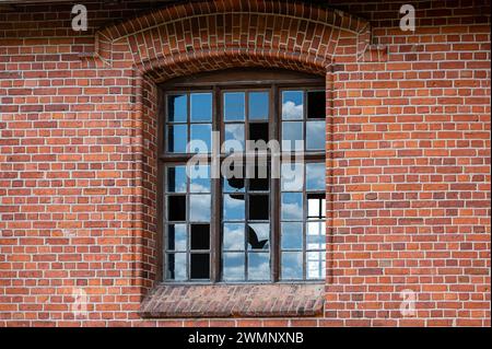 An old window with broken glass panes in a red brick wall. Close-up Stock Photo