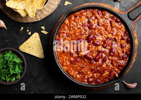 Chili con carne in cast iron pan on black background close up. Homemade mexican food, chili with red beans and ground beef, protein fiber meal. Stock Photo