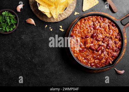Chili con carne in cast iron pan on black background, top view, copy space. Homemade mexican food, chili with red beans and ground beef, protein fiber Stock Photo