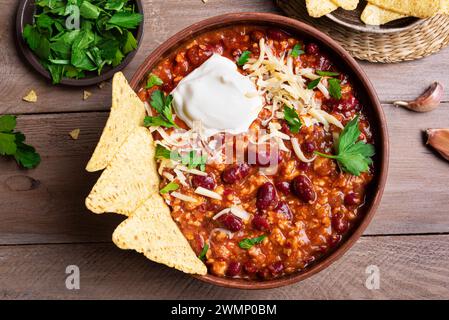 Chili con carne with cheese topings and nachos on wooden background, top view. Homemade mexican food, chili with red beans and ground beef. Chilean be Stock Photo